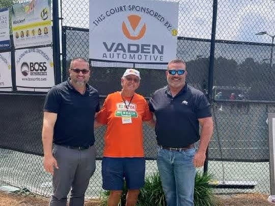Three people standing together in front of tennis courts